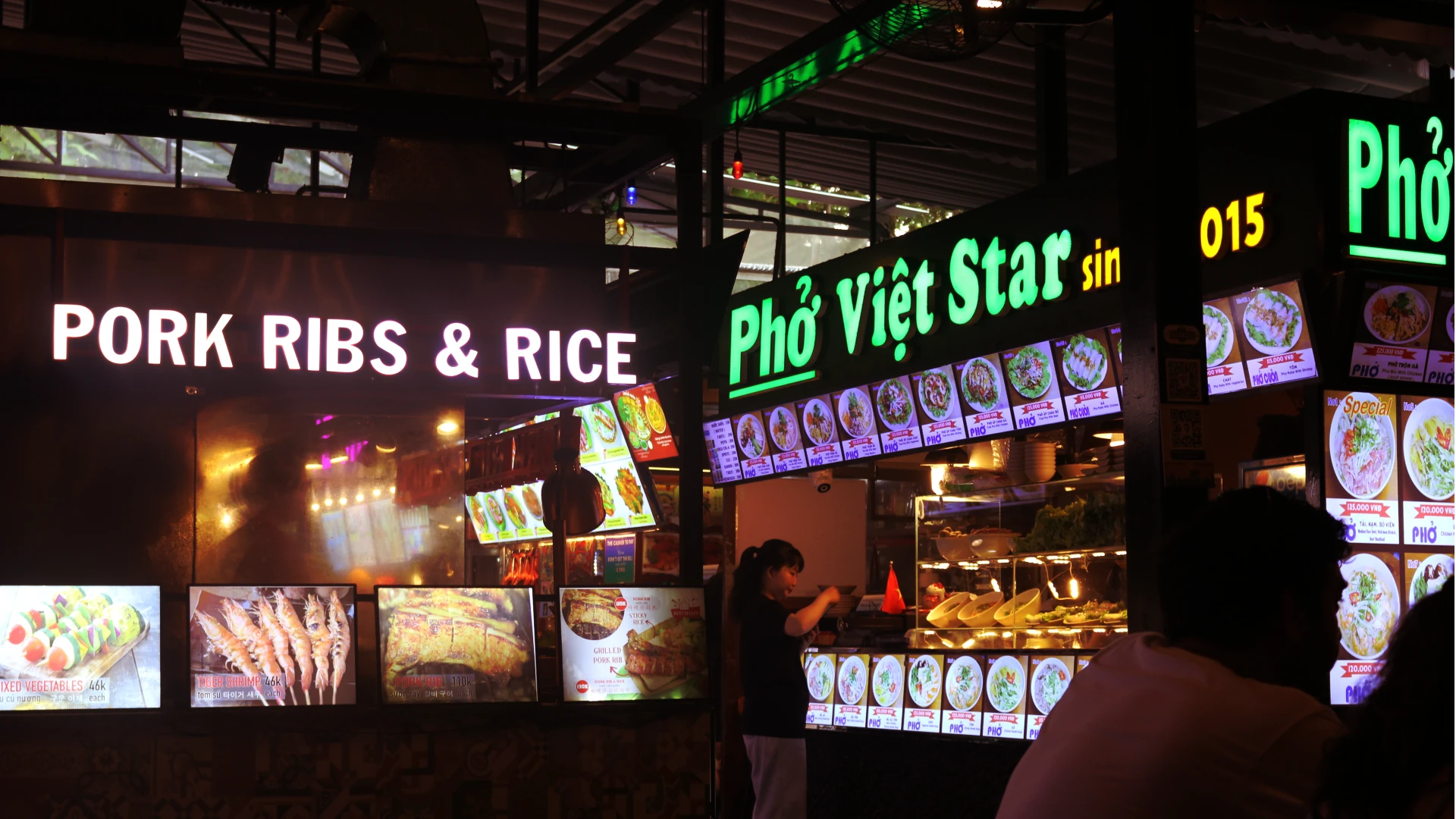 neon lights in a food market that read 'pork ribs and rice' and 'pho viet star'